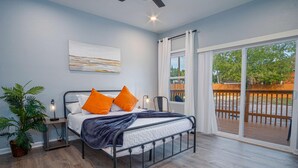 Ein Schlafzimmer mit einem Bett, einem Nachttisch, einer Topfpflanze und einem Fenster mit Blick auf eine Terrasse.