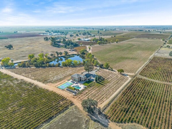 An aerial view of a property with a large house, tennis court, swimming pool, and surrounding agricultural fields.