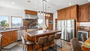 Una cocina moderna con armarios de madera, una isla central con taburetes de bar, electrodomésticos de acero inoxidable y un ventanal grande.