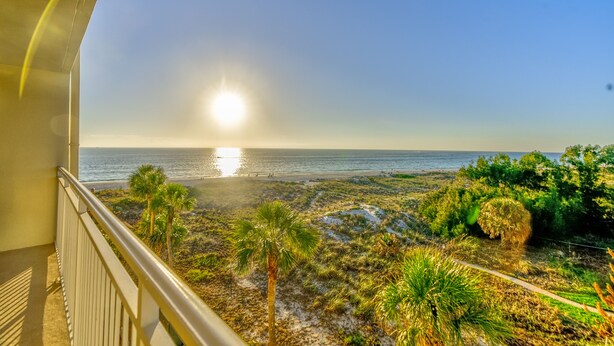 En balkon med udsigt over strand og hav i solnedgang.