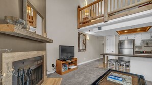 A spacious living area with a fireplace, a television, and a kitchen area with a bar. - 2BD Condo w/Ski Run Views & Hot Tub Access (Park City)