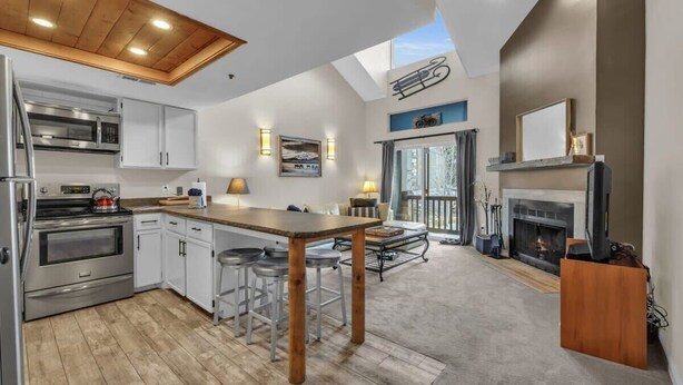 A modern kitchen with white cabinets, stainless steel appliances, and a wooden island. There is a fireplace and a balcony with a view. - 2BD Condo w/Ski Run Views & Hot Tub Access (Park City)