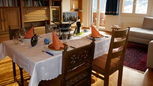 Een eethoek met een tafel gedekt voor twee personen, houten kasten, een televisie en uitzicht op de natuur door grote ramen.