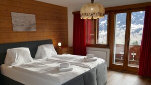Een slaapkamer met een groot bed, houten wanden, een raam met uitzicht op bergen en een rood gordijn.