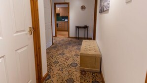A hallway with a patterned carpet, a bench, and a door leading to a kitchen area. - Elm Grove by Interhome (Inverness)