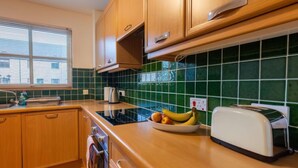 A kitchen with wooden cabinets, a black stove, a green tiled backsplash, and a toaster on the counter. - Elm Grove by Interhome (Inverness)