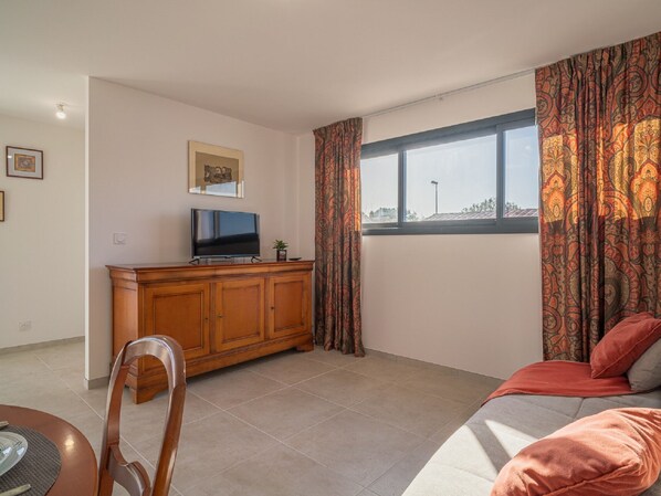 A living room with a TV on a wooden cabinet, a sofa, and a window with patterned curtains.