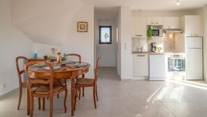 A modern kitchen with white cabinets, a microwave, and a refrigerator. There is a dining area with a wooden table and chairs.