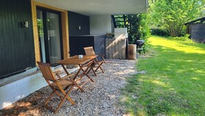 Une terrasse extérieure avec une table et des chaises, un barbecue et un coin jardin.