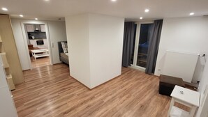 Un appartement moderne doté d’un plancher en bois, d’un coin cuisine, d’un canapé, d’une table à manger et d’une grande fenêtre avec des rideaux.