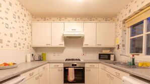A compact kitchen with white cabinets, a gas stove, a microwave, and a built-in washing machine. - Cedar House by Interhome (Inverness)