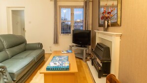 A living room with a sofa, a television, a fireplace, and a Scrabble game on the coffee table. - Cedar House by Interhome (Inverness)