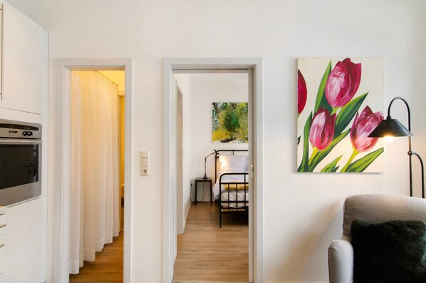 A narrow hallway with a bed, a desk, and a painting of tulips. - Apartment 'Ferienwohung 1' with Private Terrace, Balcony and Wi-Fi (Jever)