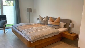 Ein modernes Schlafzimmer mit einem Holzbett, gemusterten Betttextilien, einem Nachttisch und einem Sessel.