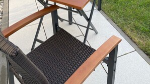Eine Terrasse im Freien mit einem Holztisch und Stühlen, umgeben von einer Rasenfläche und Bäumen.