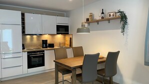 Eine moderne Küche mit weißen Schränken, einem eingebauten Backofen, einer Kaffeemaschine und einem Essbereich mit einem Holztisch und Stühlen.