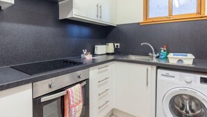 Une cuisine compacte équipée d’une cuisinière, d’un four, d’un évier et d’un lave-linge encastré.