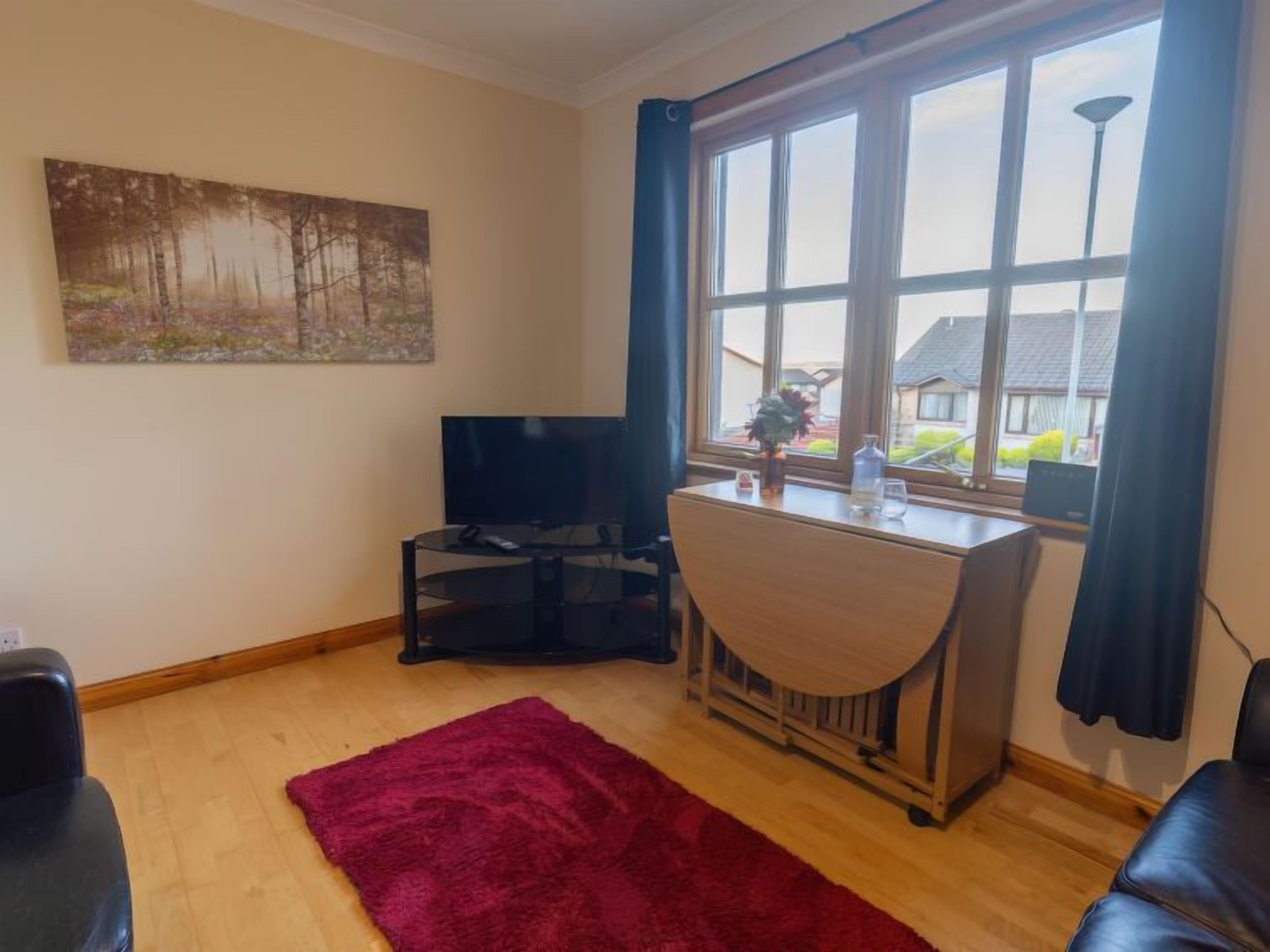 A living room with a TV, a desk, and a window with curtains.