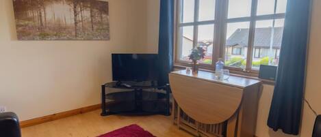A living room with a TV, a desk, and a window with curtains.