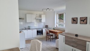 A modern kitchen with white cabinets, a dining area with a wooden table, and a window with artwork.