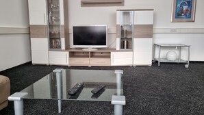 A modern living room with a flat-screen TV, glass-fronted cabinets, a coffee table, and a framed picture on the wall.