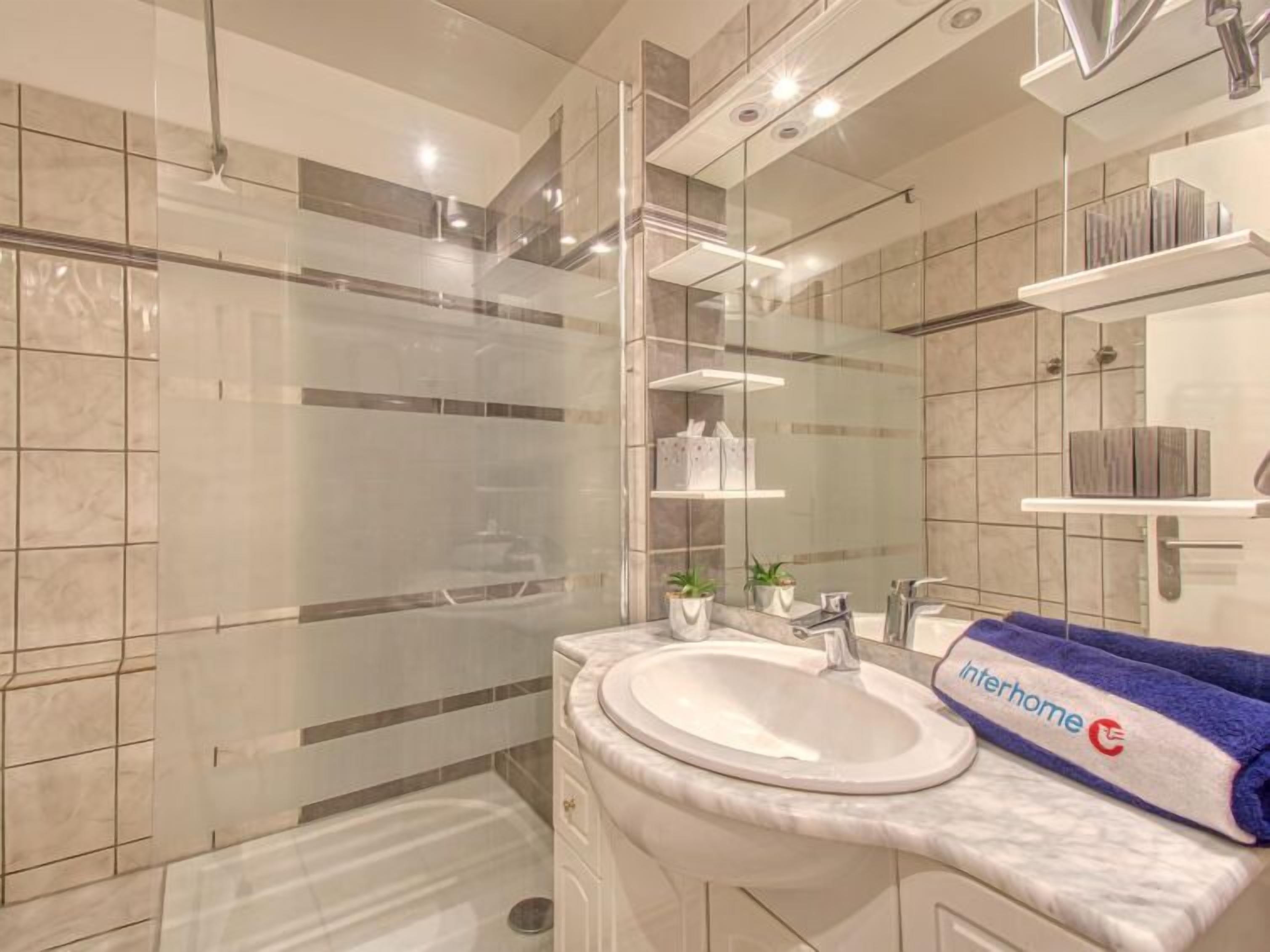 A modern bathroom with a glass shower enclosure, a marble sink, and a vanity with a towel.