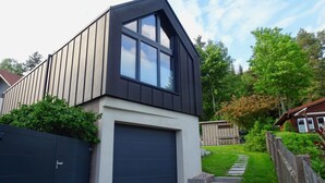 Una casa moderna con garage, tetto spiovente e giardino recintato da una staccionata di legno.