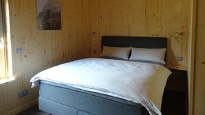 Una stanza con rivestimento in legno, un letto, una lampada a parete e un piccolo quadro.