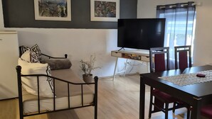 Una sala de estar con un sofá, una mesa de comedor con sillas, un televisor de pantalla plana y obras de arte en las paredes.