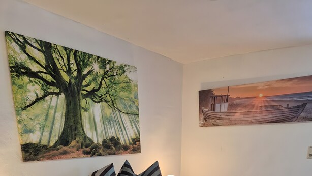 Un dormitorio con una cama, almohadones a rayas, una mesita de noche, una lámpara y dos cuadros en la pared.