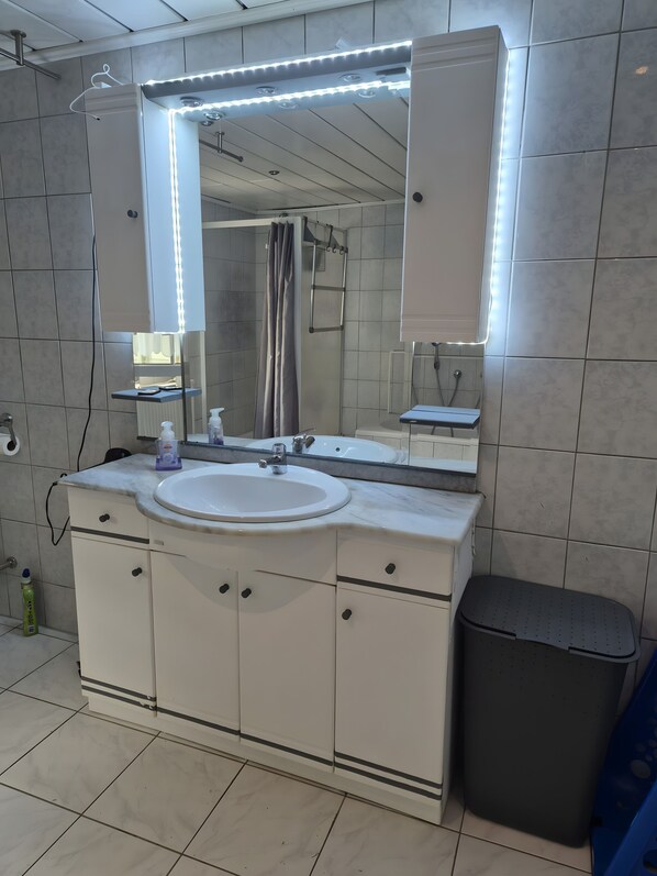 Une salle de bain équipée d’un lavabo, d’un miroir, d’un meuble-lavabo et d’une poubelle.