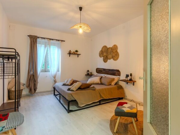 Une chambre confortable avec un lit superposé, un grand lit doté d’une tête de lit en bois, un luminaire suspendu et une décoration murale rustique.