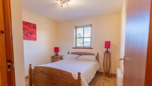 A bedroom with a wooden bed, two bedside tables with lamps, a window with blinds, and a red floral artwork on the wall. - Miller Heights by Interhome (Inverness)