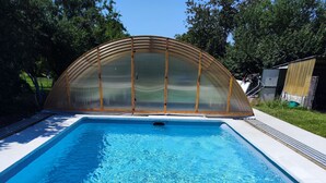 A rectangular swimming pool with clear blue water, surrounded by a wooden deck and a glass enclosure. - Chez sandrine (Gray-la-Ville)