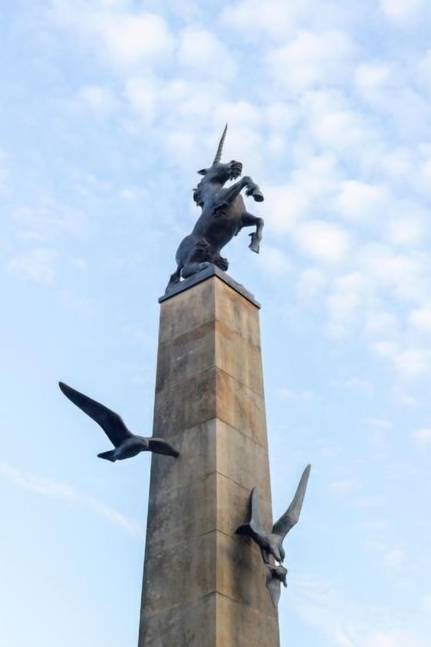 Un grand monument surmonté d’une statue d’une créature mythique, flanqué de deux sculptures d’oiseaux, une de chaque côté.