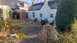 A white house with a grey roof, a wooden fence, and a stone patio with outdoor furniture. - Old Lodge by Interhome (Inverness)
