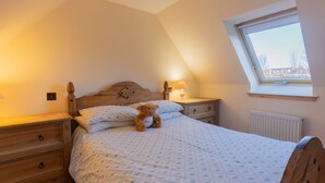 A bedroom with a sloped ceiling, a skylight, a wooden headboard, a bedside table with a lamp, a wooden dresser, and a teddy bear on the bed. - Lodge Road by Interhome (Inverness)