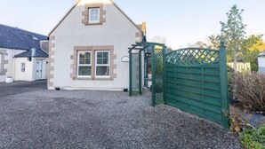 A small, single-story house with a triangular roof, a front door, and a green gate. - Lodge Road by Interhome (Inverness)