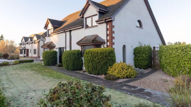 A row of modern houses with white walls and dark roofs, surrounded by well-maintained hedges and a grassy lawn. - Evergreen House by Interhome (Inverness)