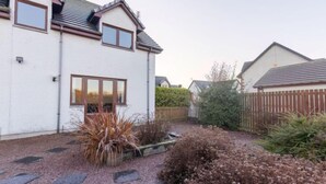 A two-story house with a white exterior, a sloped roof, and a front garden with gravel paths and various plants. - Evergreen House by Interhome (Inverness)