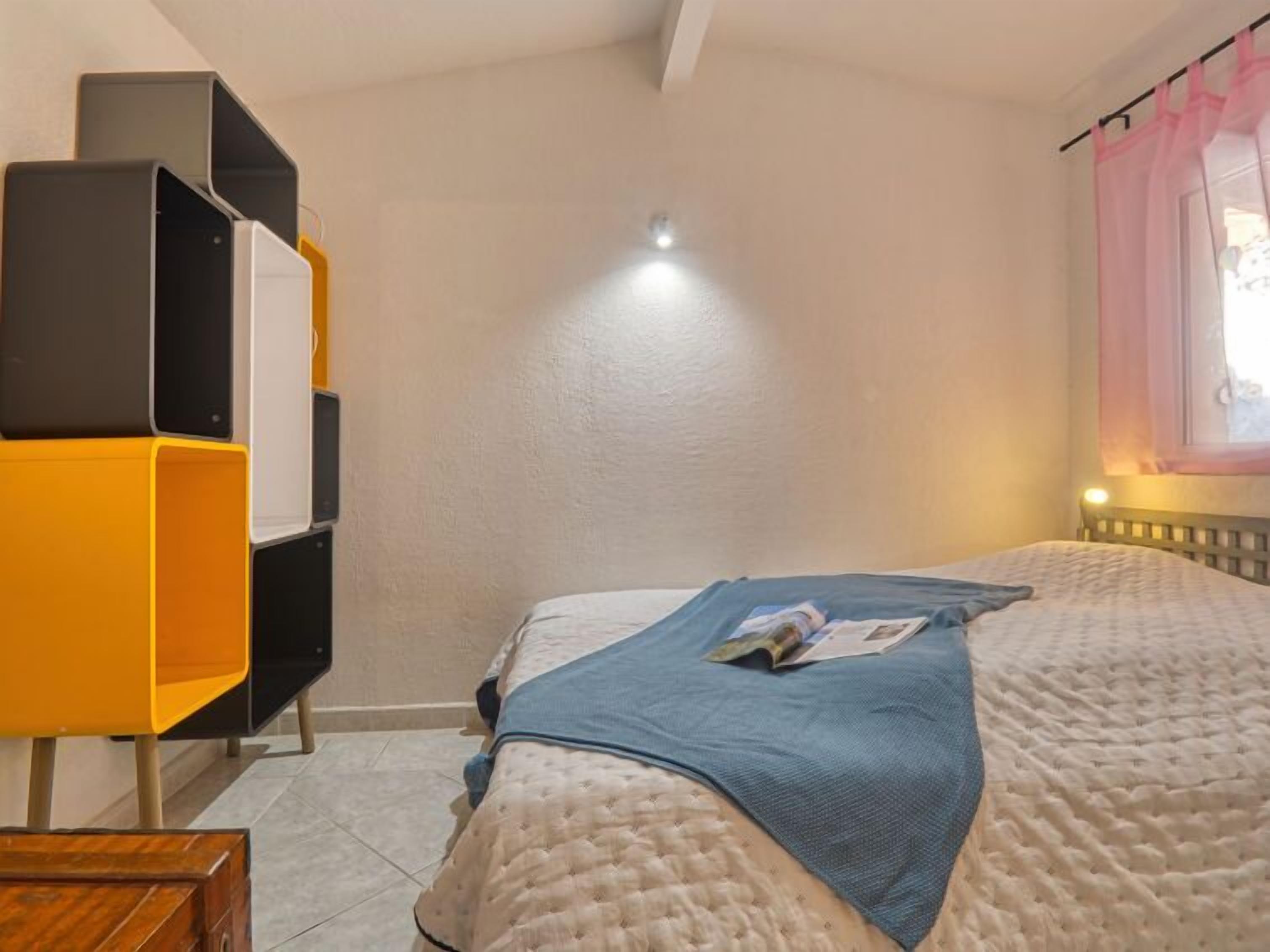 Um quarto com cama, mesa de cabeceira, estante e janela com cortinas.