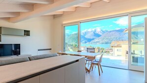 Une cuisine moderne dotée d’un grand îlot central, d’un coin repas avec une table et des chaises, et d’une grande porte-fenêtre coulissante donnant sur une vue imprenable sur les montagnes.