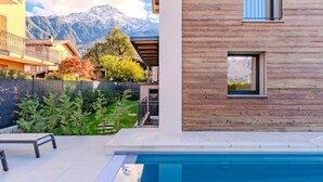 Un espace moderne aménagé autour d’une piscine, avec un bâtiment en bois, une vue sur les montagnes et un ciel dégagé.