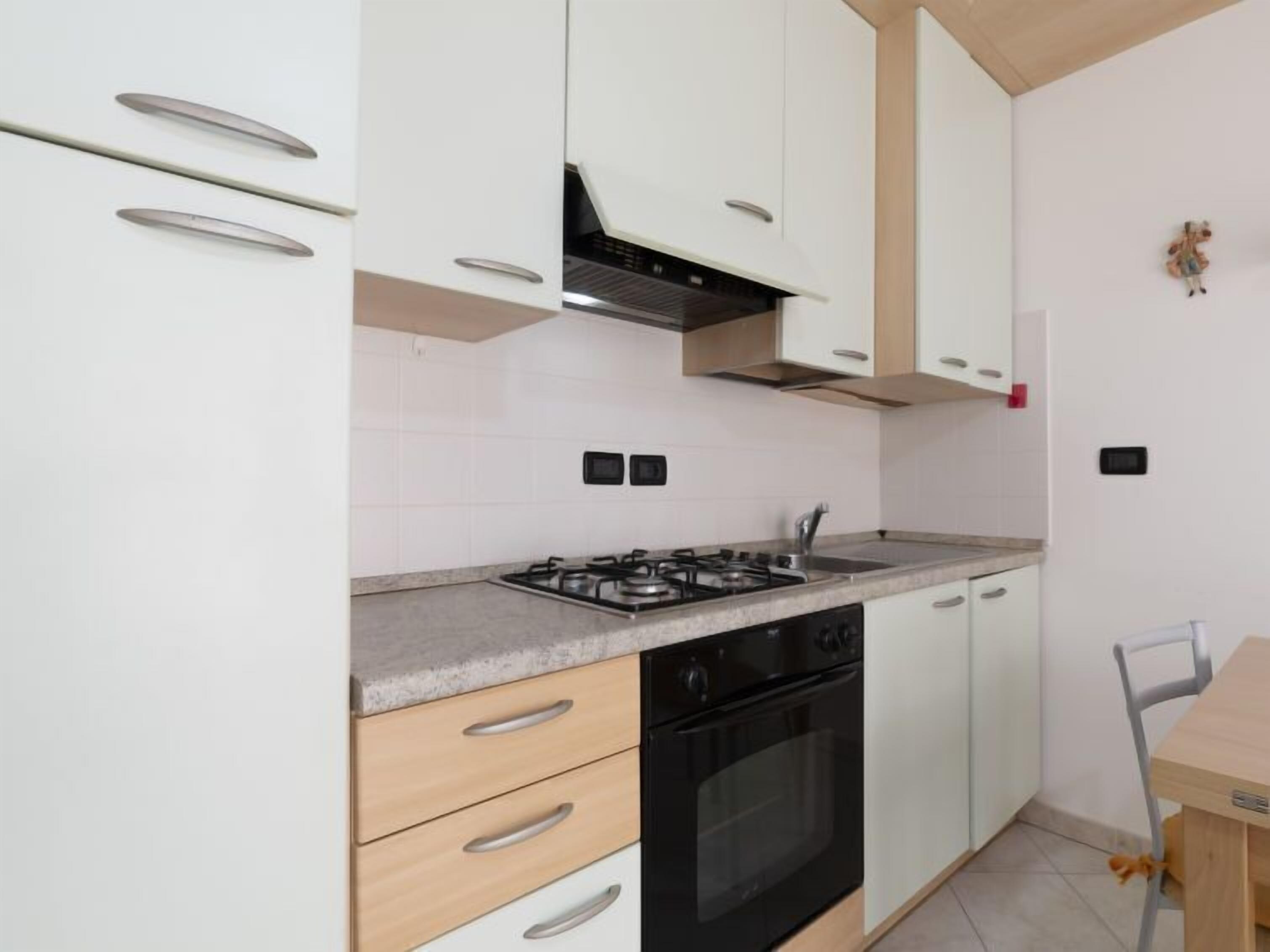 Een keuken met witte kastjes, een zwarte oven en een houten eettafel met een stoel.