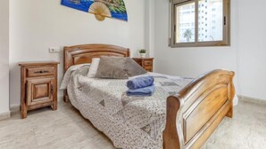 A bedroom with a wooden bed, a nightstand, a wall-mounted painting, and a window with a view of buildings. - Edificio Mirablau by Interhome (Empuriabrava)