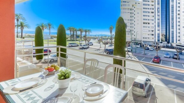 A balcony with a dining table set for two, overlooking a parking area and a building with multiple floors. - Edificio Mirablau by Interhome (Empuriabrava)