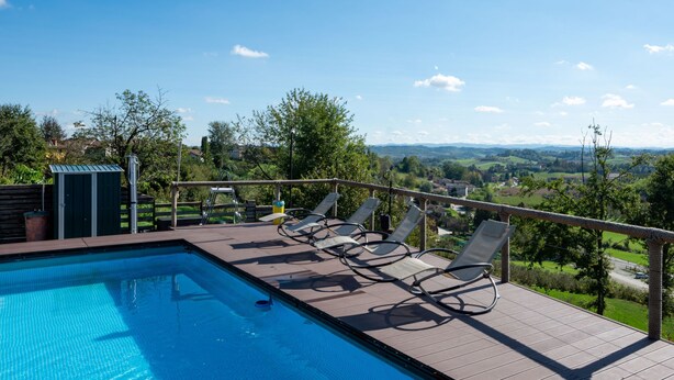 A swimming pool with lounge chairs on a deck, surrounded by greenery and a view of distant hills. - Helix1912 by Interhome (San Damiano d'Asti)