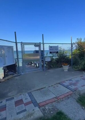 Une entrée fermée par un portail donnant accès à une plage privée, sous un ciel dégagé.
