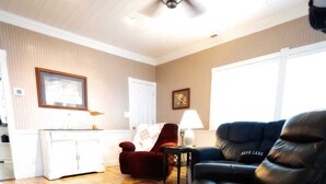 Un salon avec un plancher en bois, un canapé en cuir noir, un fauteuil rouge, un meuble blanc et un tapis coloré.