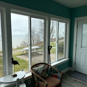 A room with a view of the lake, a wicker chair, a small table, and a door.